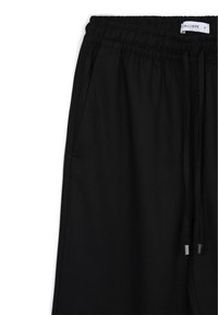 Pantaloni della tuta neri con vita elasticizzata, laccetto con punte metalliche e tasche laterali. Il tessuto ha una texture liscia e un design minimale.