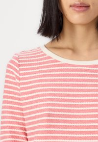 Randig långärmad topp i korall och kräm, med rund halsringning och textil med växlande vågiga ränder.