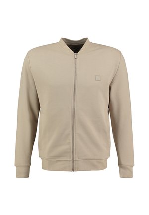 Giacca beige con zip, colletto rotondo, tessuto texturizzato, tasche laterali e una piccola patch con logo sul petto. Finitura liscia.