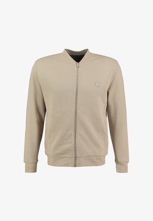 Giacca beige con zip, colletto rotondo, tessuto texturizzato, tasche laterali e una piccola patch con logo sul petto. Finitura liscia.