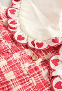 Țesătură roșie cu modele în formă de inimă și margini ondulate, având un închizător din lemn pe un fundal crem.