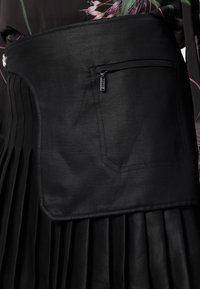 Gonna plissettata nera con una vita textured. Presenta una tasca con zip e cuciture ad accentuazione curva sul lato sinistro.