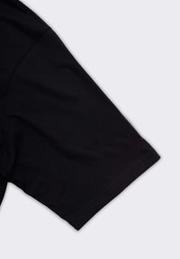 Maglietta nera a maniche corte in cotone con cuciture visibili su sfondo grigio neutro.