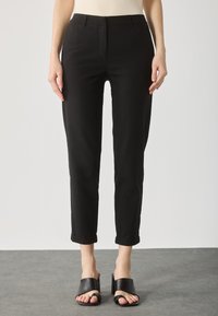 Sorte slim-fit bukser med en glat tekstur, cropped længde og opbrettede manchetter, kombineret med sorte åbne slides.