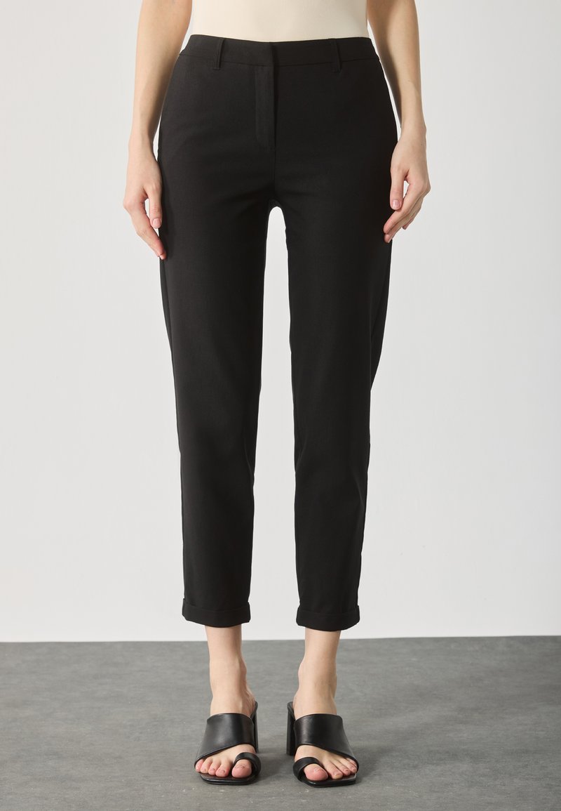Sorte slim-fit bukser med en glat tekstur, cropped længde og opbrettede manchetter, kombineret med sorte åbne slides.