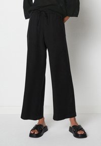 Zwarte wijde broek met een elastische tailleband en een trekkoord. Lichtgewicht stof, gladde textuur. G gecombineerd met zwarte sandalen met banden.