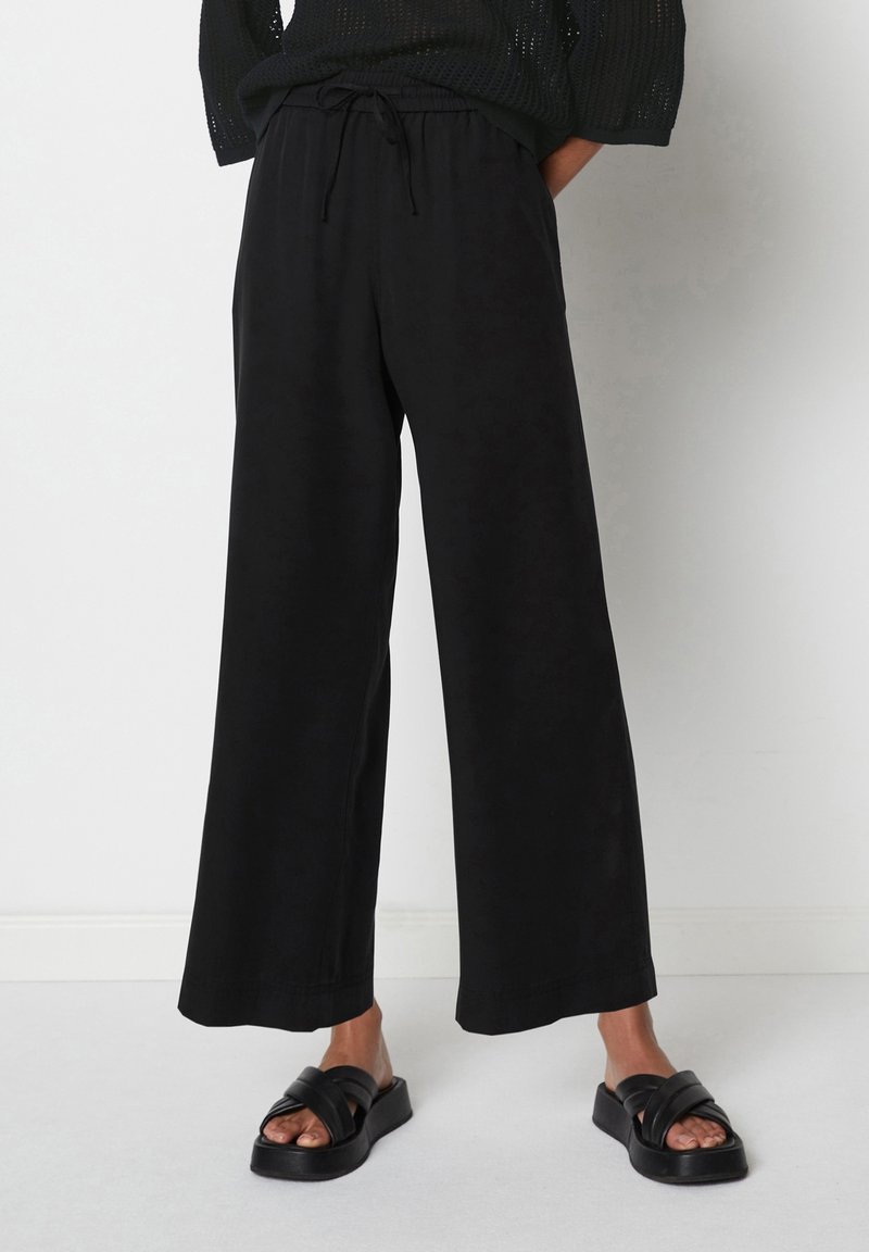 Zwarte wijde broek met een elastische tailleband en een trekkoord. Lichtgewicht stof, gladde textuur. G gecombineerd met zwarte sandalen met banden.
