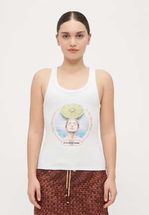 Top bianco senza maniche con una stampa grafica di una donna e un lime sopra la sua testa. Presenta del testo incorniciato in arancione e blu, che enfatizza un tema tropicale.
