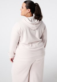 Lichtroze hoodie met ribbeltextuur, een relaxte pasvorm en lange mouwen, gecombineerd met bijpassende wijde broek. Eenvoudig ontwerp.