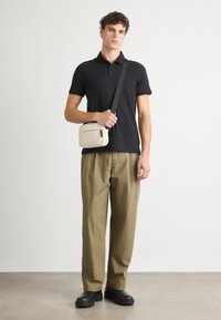 Čierne polo tričko, voľné khaki nohavice a čierne robustné topánky. Svetlo béžová crossbody taška so zipsom. Hladké textúry a neformálny dizajn.