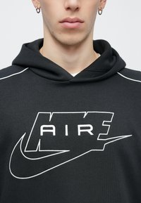 Zwarte hoodie met een wit geborduurd "AIR"-logo en een Nike-swoosh. Voorzien van een capuchon en witte accentstiksels langs de schouders.