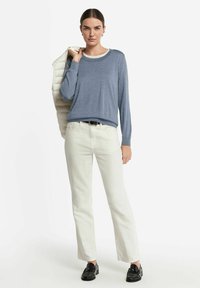 Ljusblå tröja i mjukt stickat material, kombinerad med vita raka byxor och svarta loafers. Tröjan har en kontrasterande ringning.