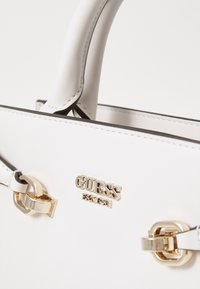 Borsa a mano bianca in pelle con dettagli in hardware dorato, caratterizzata da un logo prominente, una texture liscia e un piping nero a contrasto lungo i bordi.