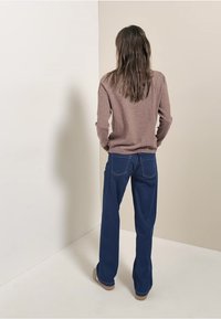 Brązowy sweter z okrągłym dekoltem, w połączeniu z ciemnoniebieskimi dżinsami w kształcie dzwonów z tylnymi kieszeniami i kontrastowym przeszyciem.