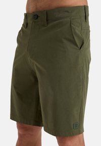 Pantaloni shorts verde oliva con design frontale piatto, chiusura con bottone, tasche laterali e sottile patch con logo sulla parte inferiore della gamba. Tessuto liscio e leggero.