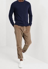 Mörkblå tröja med långa ärmar kombinerad med ljusbruna manchesterbyxor och vita sneakers. Tröjan har en klassisk rund halsringning.