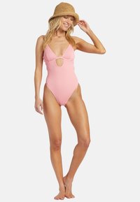 Lyserød ribbet én-dels badesuit med dyb V-udskæring og cirkulært udskæring ved brystet. Teksturen fremstår blød med en tætsiddende design.