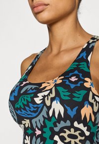 Πολύχρωμο φανελάκι με εφαρμοστό σχέδιο λουλουδιών σε μαύρο φόντο, με φαρδιές τιράντες και στρογγυλή λαιμόκοψη. Μαλακό, υφή υφάσματος.