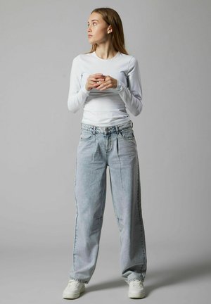 Biały top z długim rękawem połączony z jasnoniebieskimi, luźnymi dżinsami z wyblakłymi plamami i delikatnym przecieraniem, uzupełniony białymi trampkami.