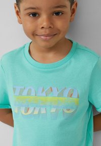 Türkisfarbener Baumwoll-T-Shirt mit kurzen Ärmeln, das ein mehrfarbiges "TOKYO"-Grafikdesign, einen gerippten Rundhalsausschnitt und eine weiche Textur aufweist.