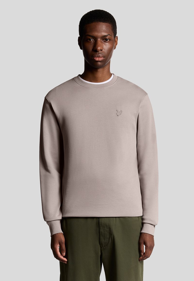 Licht taupe sweatshirt met lange mouwen, ronde hals en subtiele geborduurde logo op de borst. Zachte textuur en aangesloten ontwerp.