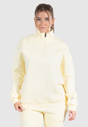 Gul zip-hals sweatshirt i blødt stof, med dropped shoulders, ribstrikkede cuffs og logo detalje på brystet, parret med matchende underdele.