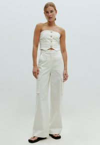 Witte cropped strapless top met knopen aan de voorkant, gecombineerd met witte wijde cargo pants met zijzakken en een gestructureerde stof.