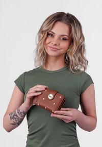 Brown leather wallet with gold accents and silver studs, featuring a flap closure and embossed logo. Compact, rectangular design.