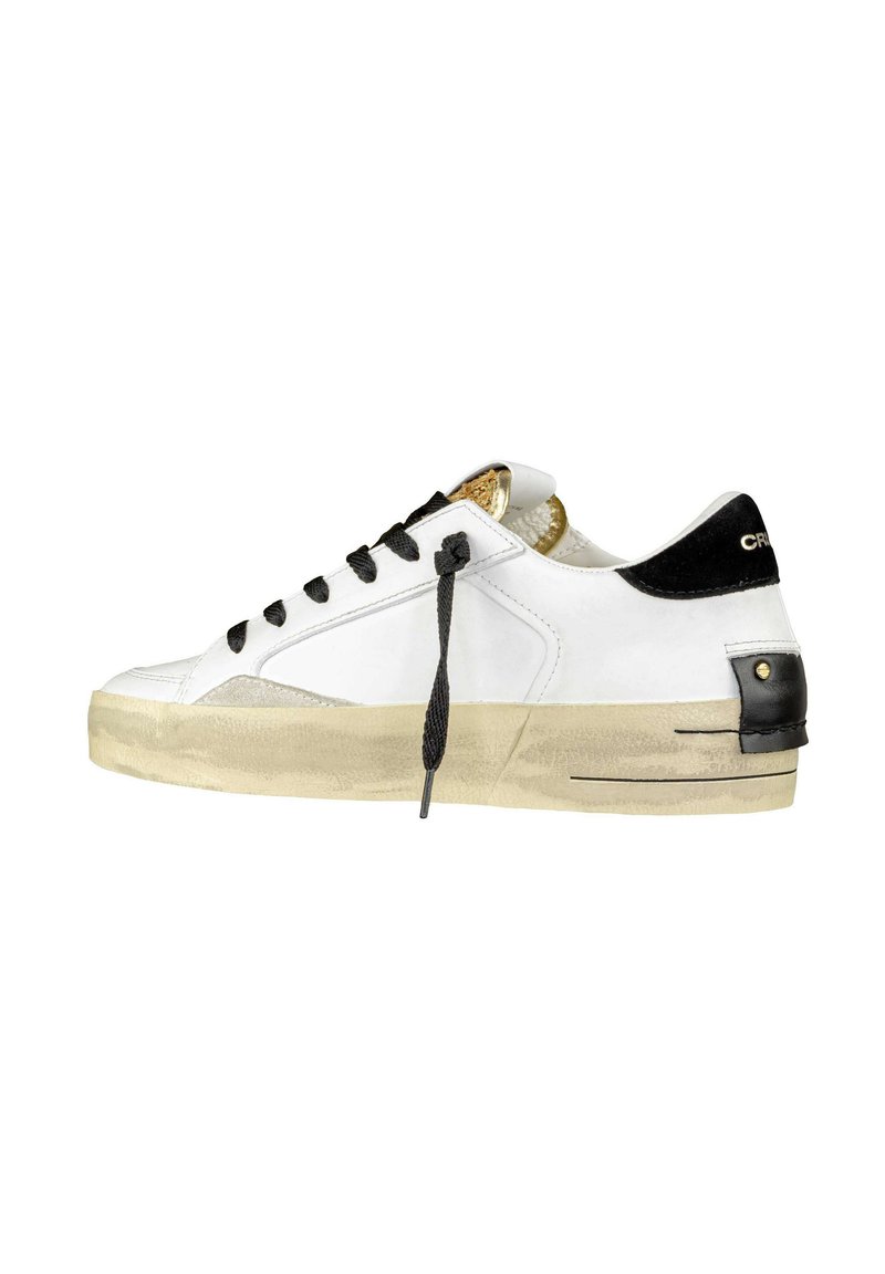 Baskets en cuir blanc avec des accents noirs, design à lacets, détails dorés sur la languette, semelle texturée et finition lisse.