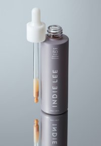 Sunscreen dropper bottle in muted grey with white textured lid; contains amber liquid; printed label with SPF 50 and brand name "INDIE LEE."