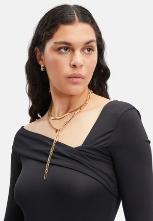 Zwarte longsleeve top met een gedrapeerde halslijn, voorzien van gelaagde gouden kettingen in verschillende stijlen.