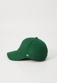 Žalias beisbolo kepurė su išlenktu kraštu, turinti iškilų siuvinėtą logotipą ir nedidelį baltą prekės ženklo detalę ant šono.