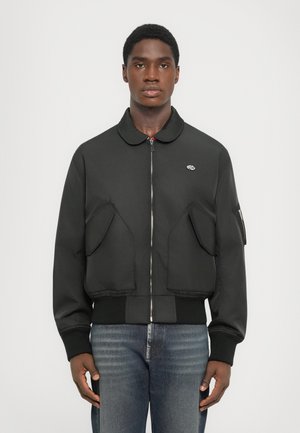 Black bomber jacket with a collar, front zipper, large patch pockets, ribbed cuffs, and hem. Material is smooth with a matte finish.