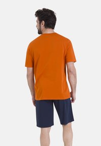 T-shirt en coton orange à manches courtes, associé à un short bleu marine. Le t-shirt est uni avec un col rond classique.