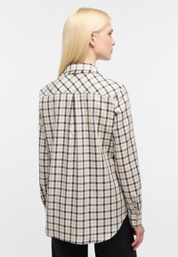 Camicia a quadri in beige, blu navy e bianco, con colletto classico, piega posteriore e maniche lunghe con polsini. Texture in cotone liscio.