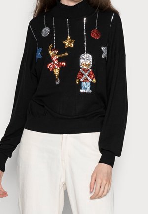 Pull noir avec des ornements suspendus en sequins : une ballerine, un soldat, des étoiles et des cercles colorés.
