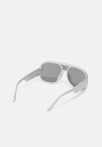 Lunettes de soleil avec une monture argentée mate, de forme rectangulaire, verres gris foncé et branches fines arborant un discret marquage à l'intérieur.