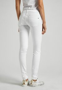 Vita smala jeans med bakfickor och subtila sömnadsdetaljer, kombinerade med vita sneakers som har guldaccenter och en strukturerad sula.