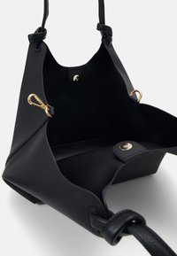 Black leather tote bag with a textured surface, gold hardware, interior pocket, and wide opening design. Adjustable strap included.