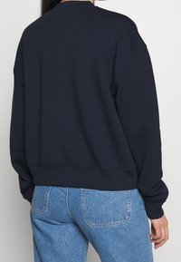 Felpa oversize blu navy in misto cotone, con scollo rotondo e polsini a costina, abbinata a jeans in denim azzurro.