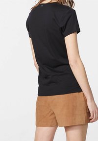 Camiseta negra de manga corta con cuello redondo, hecha de tela suave. Presenta un pequeño detalle de logo en la parte de atrás. Combinada con pantalones cortos de color marrón claro.