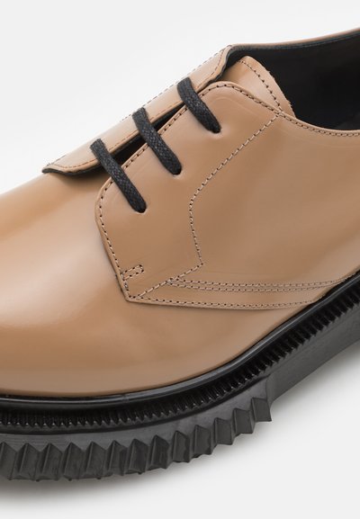 Beige nahast kingad mustade paeltega, millel on tikandiga detail ja paks, sakiline must tald kontrasti jaoks. Klassikaline disain, sile tekstuur.