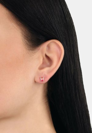 Ohr mit glattem schwarzen Haar, das einen kleinen rechteckigen Ohrring aus rosa Edelstein trägt, vor einem neutralen Hintergrund.