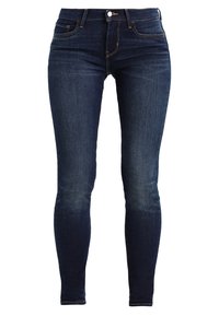 Jeans ajustados de denim azul oscuro, con un clásico diseño de cinco bolsillos, costuras acolchadas y cierre delantero con botón.