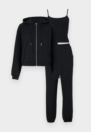 Conjunto de ropa de descanso negro de tres piezas con sudadera con capucha con cremallera, top de tirantes finos y pantalones jogger con cintura elástica sobre un fondo liso.