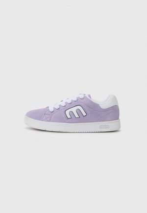Fioletowy zamszowy sneaker z białą gumową podeszwą, białymi sznurowadłami i wyraźnym logo po boku w kontrastowej białej obwódce.