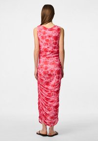 Rožu maxi kleita ar ziedu rakstu. Iezīmējas ar drapējumu detaļām aizmugurē, bez piedurknēm un pieguļošu siluetu. Valkātas plakanas sandales.