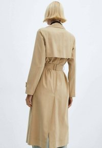 Beżowy płaszcz trench z paskiem w talii, z tylnym klapą, długimi rękawami i szwem na końcu. Gładki, lekki materiał.