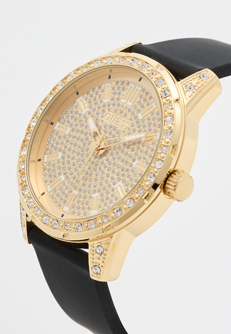 Reloj analógico en tono dorado con un bisel adornado con cristales, esfera dorada texturizada y correa de silicona negra. Presenta marcadores de hora audaces y corona.