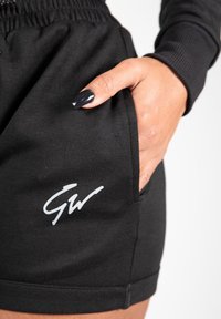 Zwarte katoenen shorts met een elastische tailleband, voorzien van een zijzak en een wit logo aan de voorkant. Gladde textuur, relaxte pasvorm.